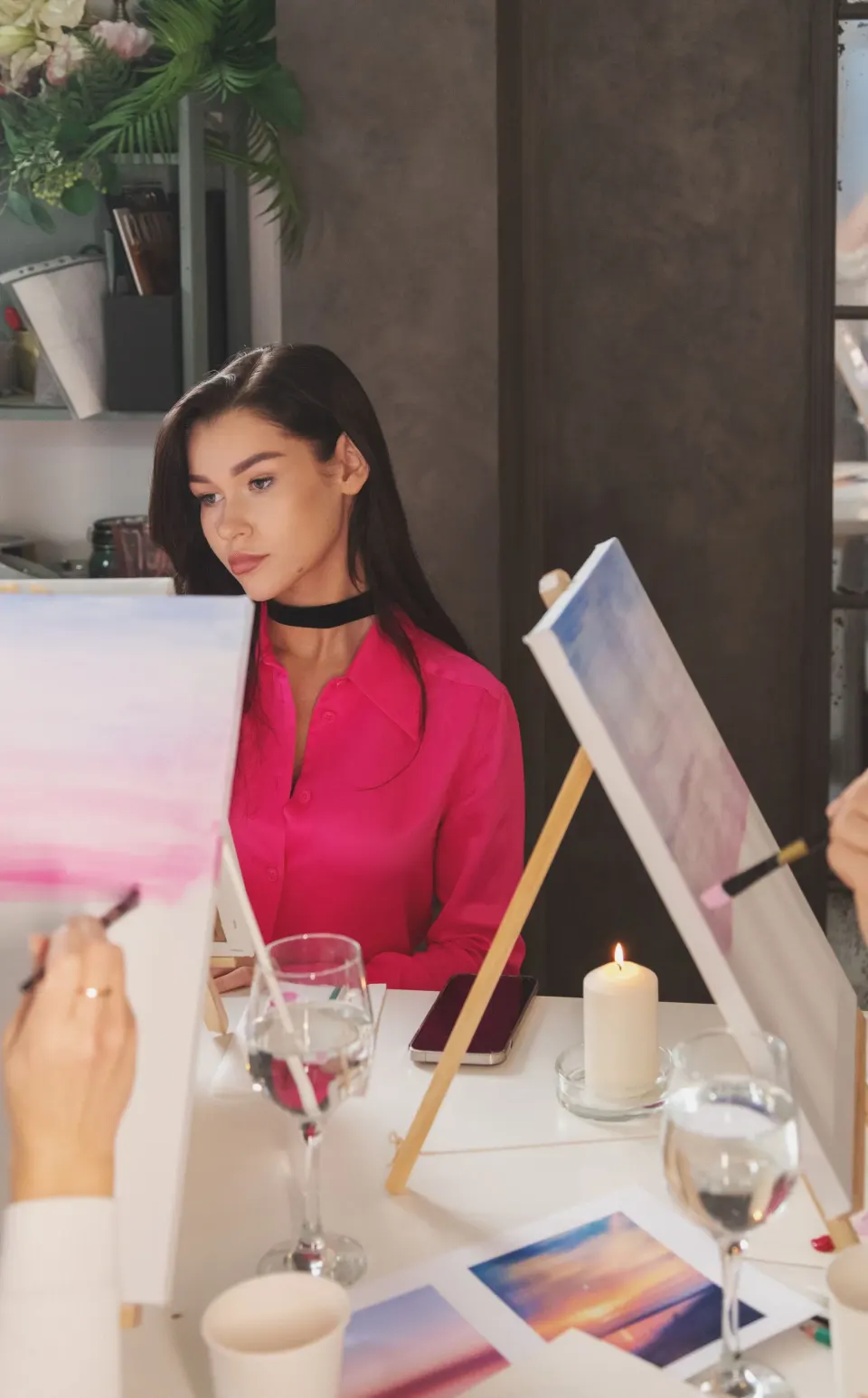 People painting pastel skies on canvases at a table during an art class